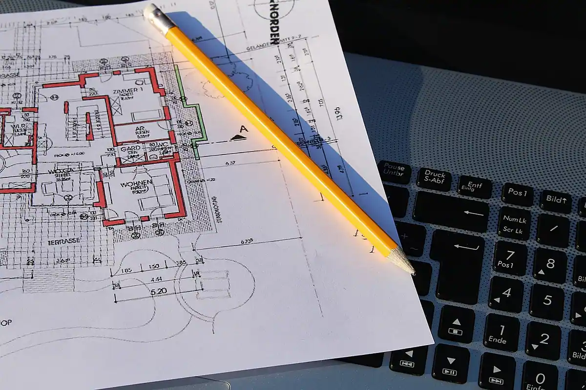 Plano de una vivienda y un lápiz sobre el teclado de un portátil, papeles que se preparan para tramitar el boletín eléctrico