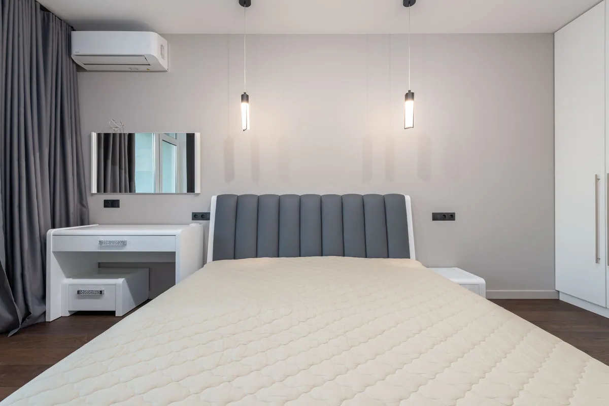 Dormitorio con un split de aire acondicionado en lo alto de la pared, cuyo filtro conviene limpiar antes del verano