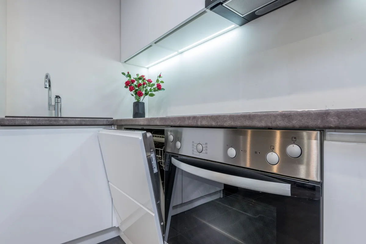 Cocina con horno empotrado, lavavajillas integrado con la puerta entreabierta, placa y campana bajo los muebles altos