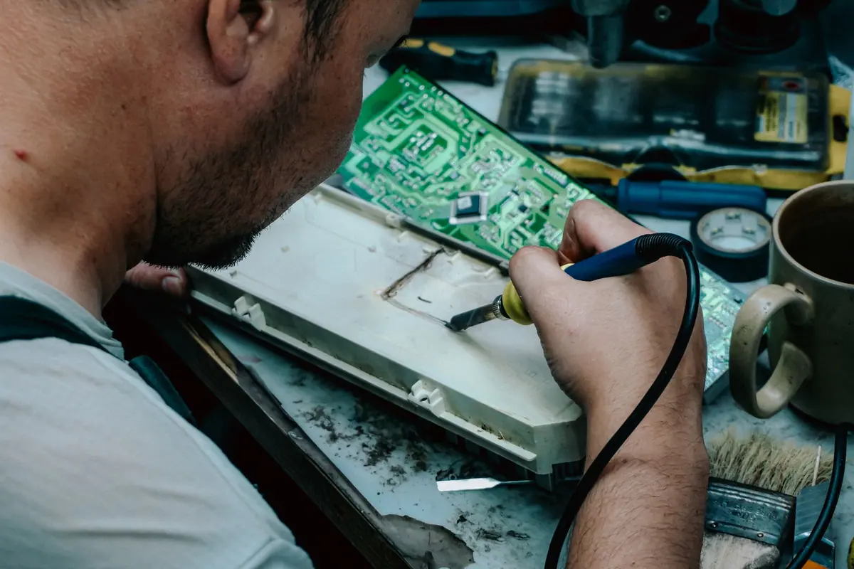 Profesional reparando con un soldador la placa electrónica de un aparato sobre un banco de trabajo