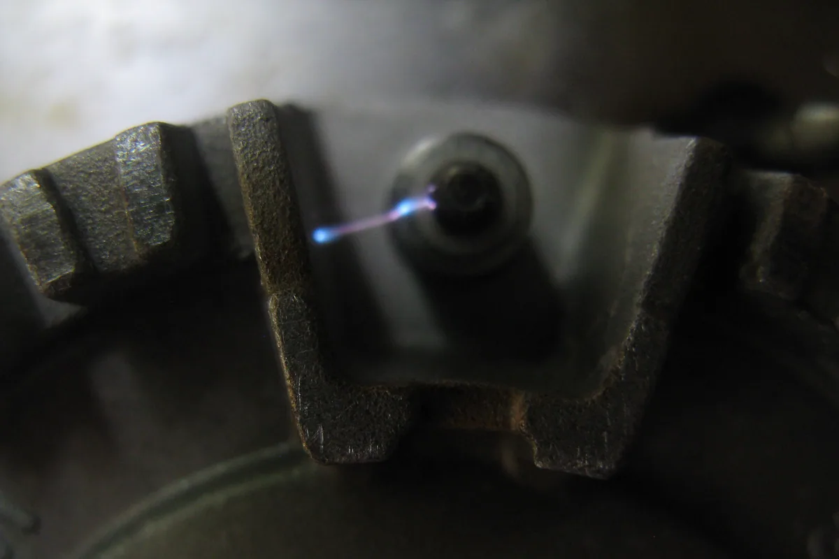 Chispa de la bujía de encendido junto a la corona del quemador de una cocina de gas