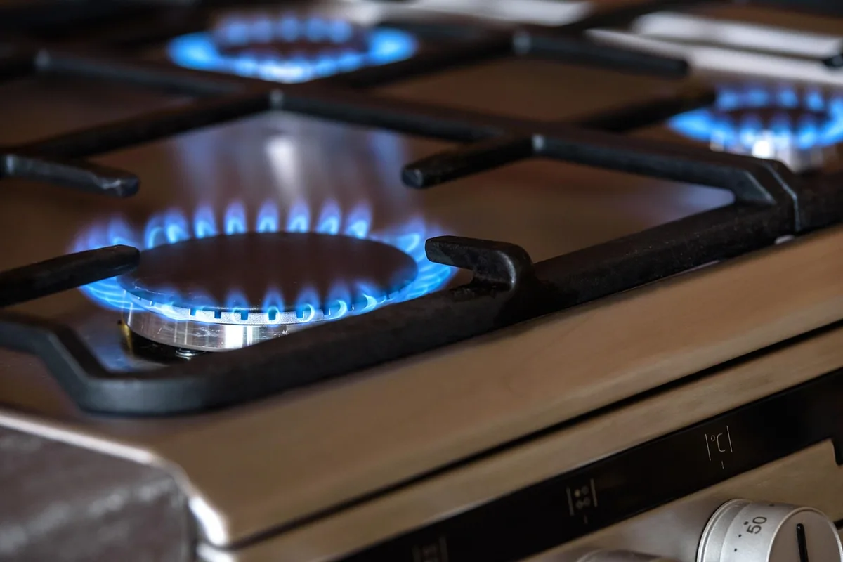 Cocina de gas de pie con tres fuegos encendidos y, debajo, los mandos del horno
