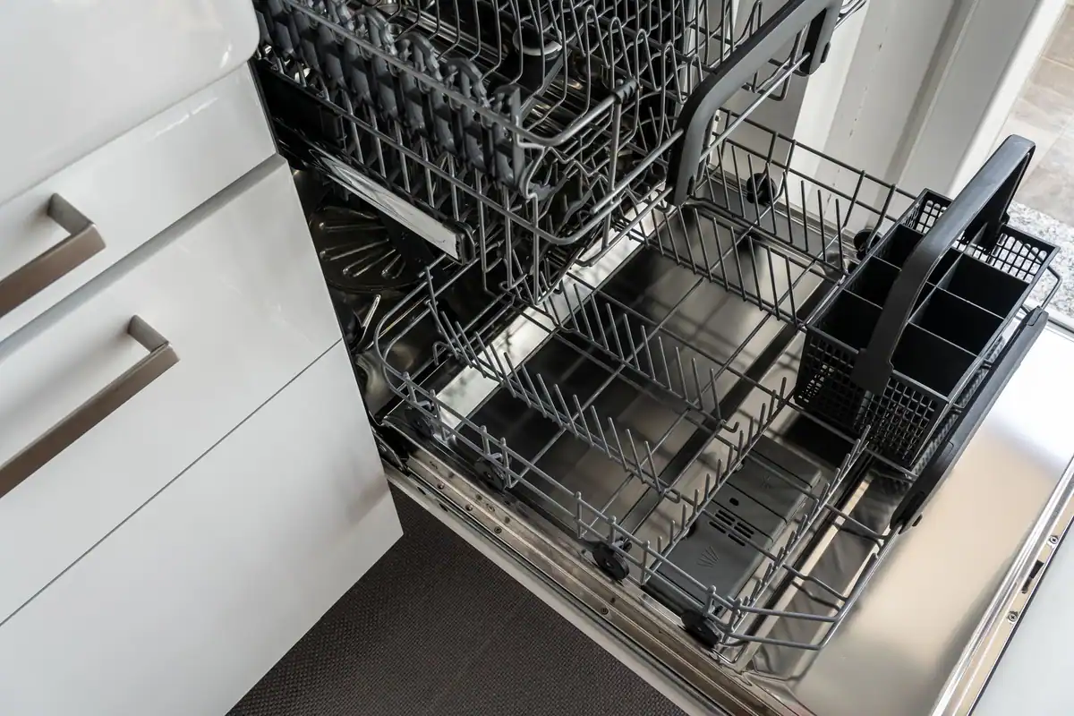 Lavavajillas integrado con la puerta abierta y las bandejas fuera, en una cocina de muebles blancos