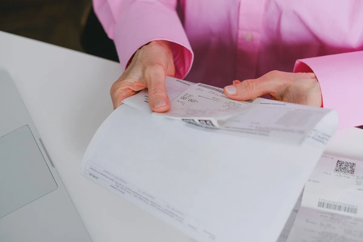 Manos revisando una factura y un tique de compra sobre una mesa, a mano para consultar la garantía