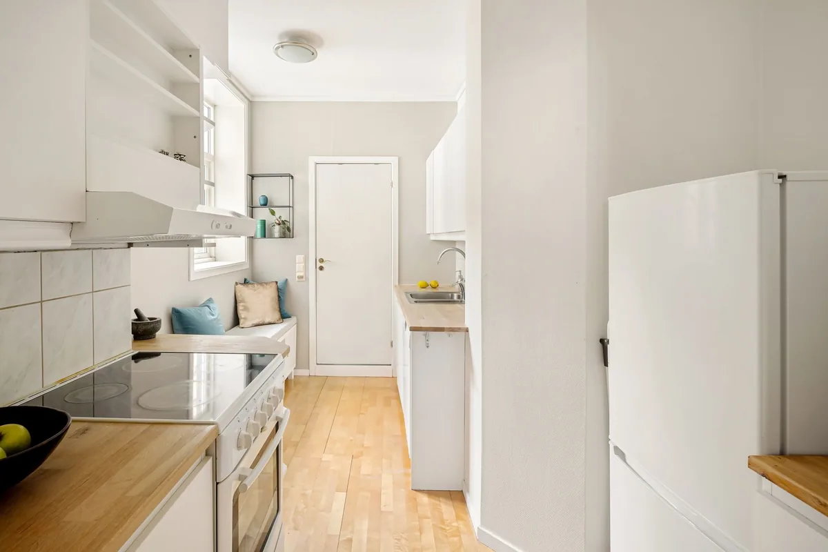 Cocina pequeña y alargada con una cocina eléctrica blanca de placa vitrocerámica y horno bajo la campana