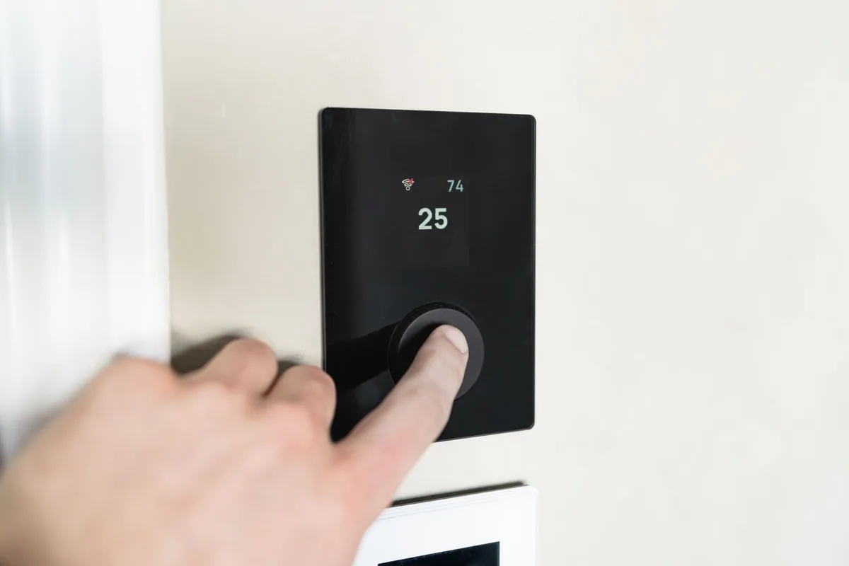 Mano pulsando el mando digital de pared que muestra la temperatura elegida