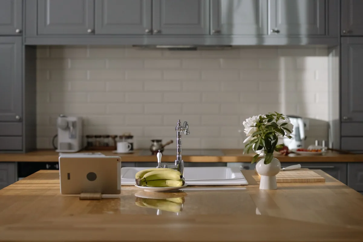 Tableta en un soporte sobre la isla de madera de una cocina, junto al fregadero y un plato de plátanos