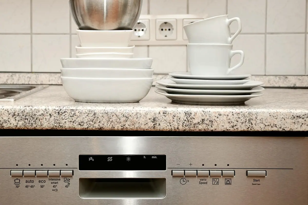 Panel de mandos de acero de un lavavajillas, con platos, cuencos y tazas limpios apilados en la encimera