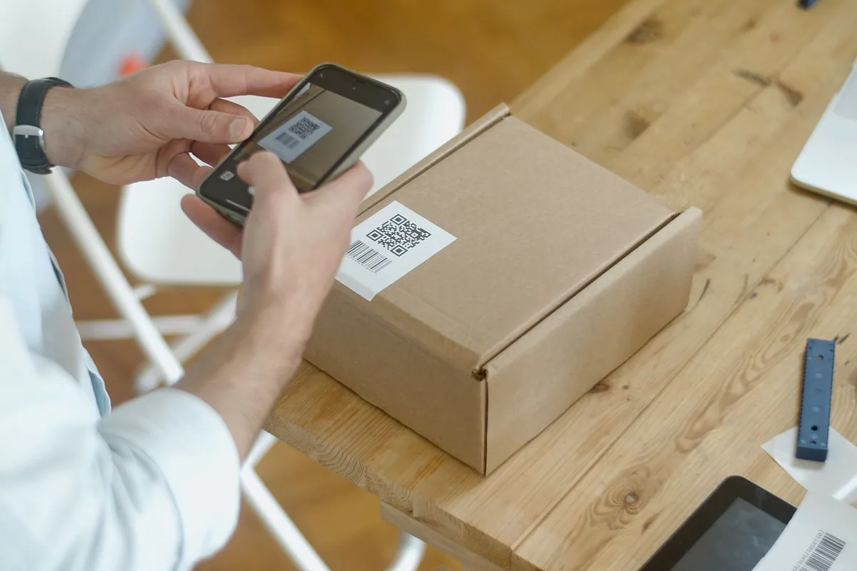 Manos fotografiando con el móvil la etiqueta con código de barras de una caja