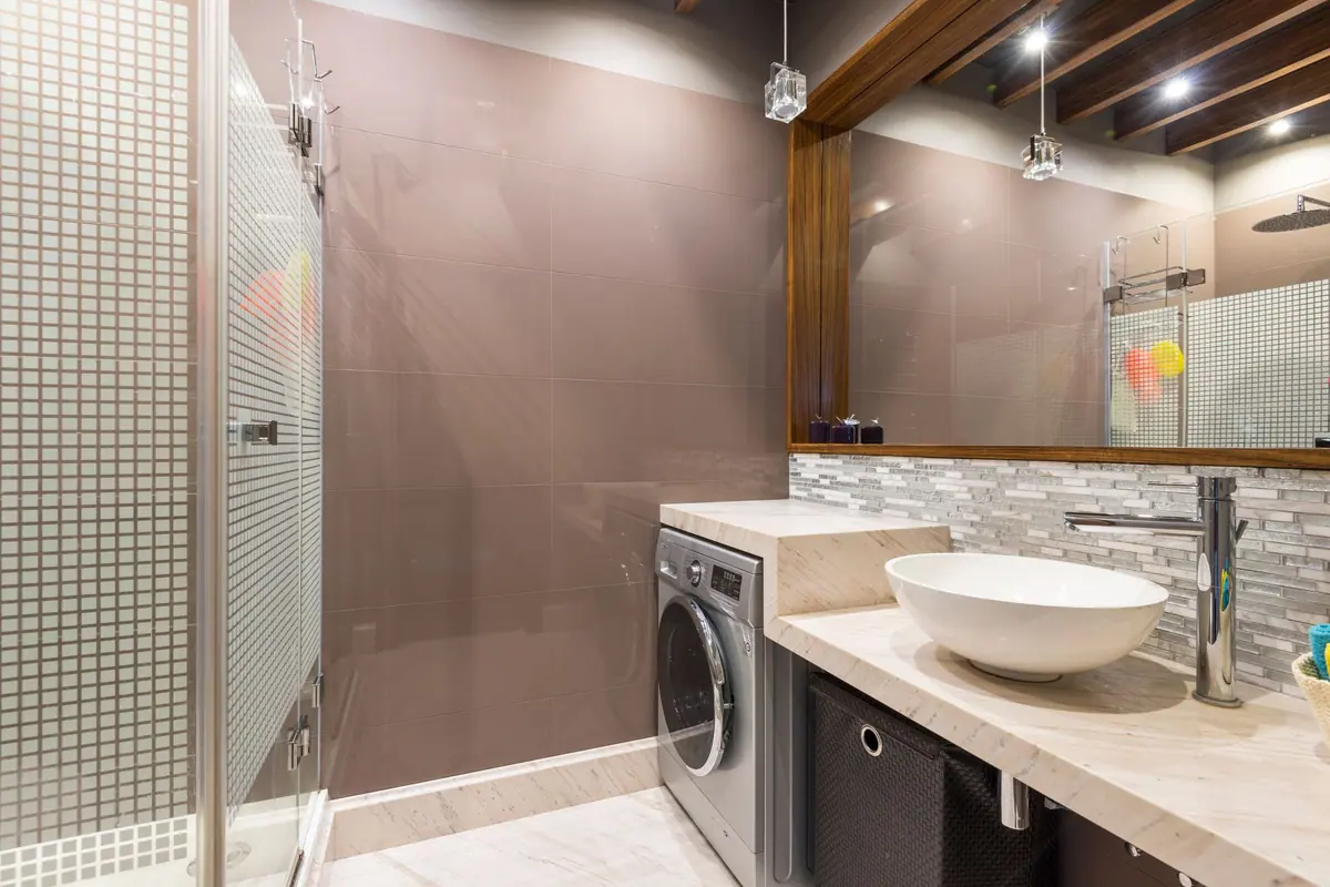 Lavadora de carga frontal encajada bajo la encimera de mármol de un baño, junto al lavabo