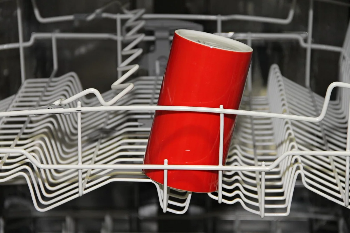 Cesta de un lavavajillas abierto, con un vaso rojo boca abajo entre las varillas