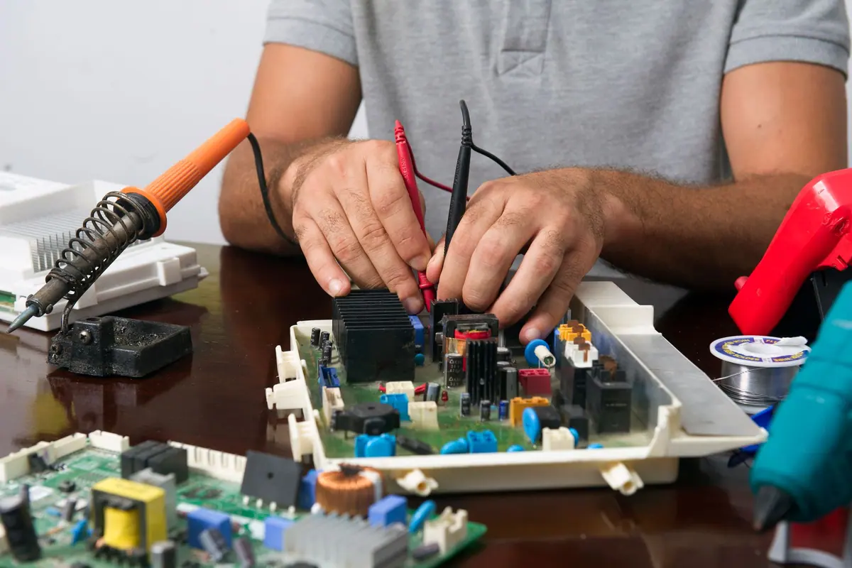 Placa electrónica de control de una lavadora fuera del aparato, comprobada con las puntas de un polímetro