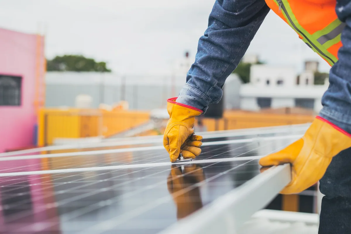 Manos con guantes de trabajo sujetando una placa solar en una azotea