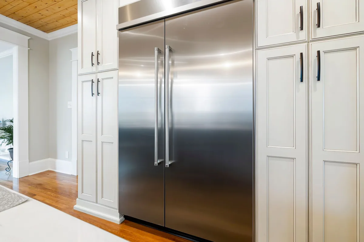 Frigorífico americano de acero inoxidable con dos puertas verticales, encastrado entre muebles de cocina blancos