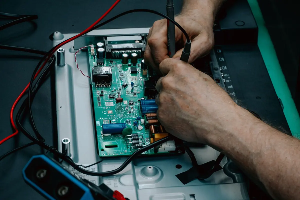 Manos de un técnico midiendo con un polímetro la placa electrónica de un electrodoméstico
