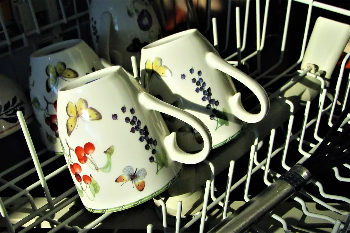 Tazas de porcelana colocadas boca abajo en la cesta de un lavavajillas abierto