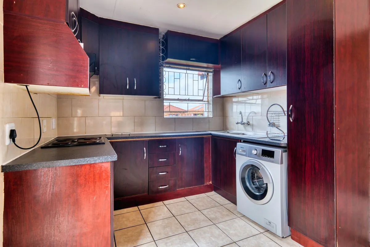 Cocina con muebles de madera oscura, placa eléctrica y una lavadora de carga frontal junto al fregadero