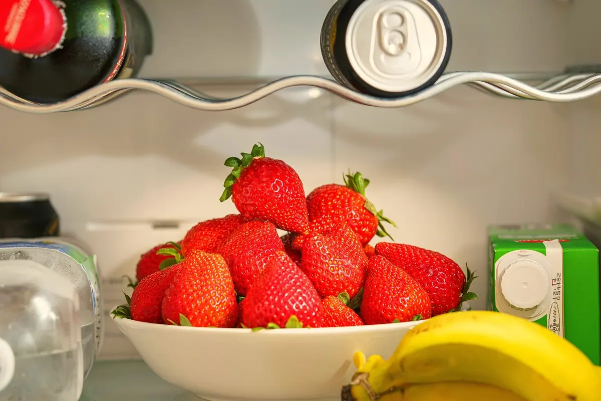 Fresas en un cuenco, plátanos y bebidas en las baldas de una nevera, alimentos frescos que hay que proteger si deja de enfriar